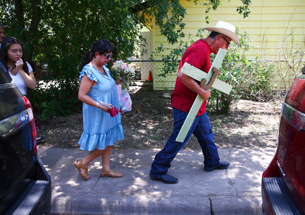 A man carries a cross he made as his wife carries flowers to pay their respects to the 21 victims of the Robb Elementary School shooting in Uvalde, Texas, Thursday, May 26, 2022. (Kin Man Hui/The San Antonio Express-News via AP)
