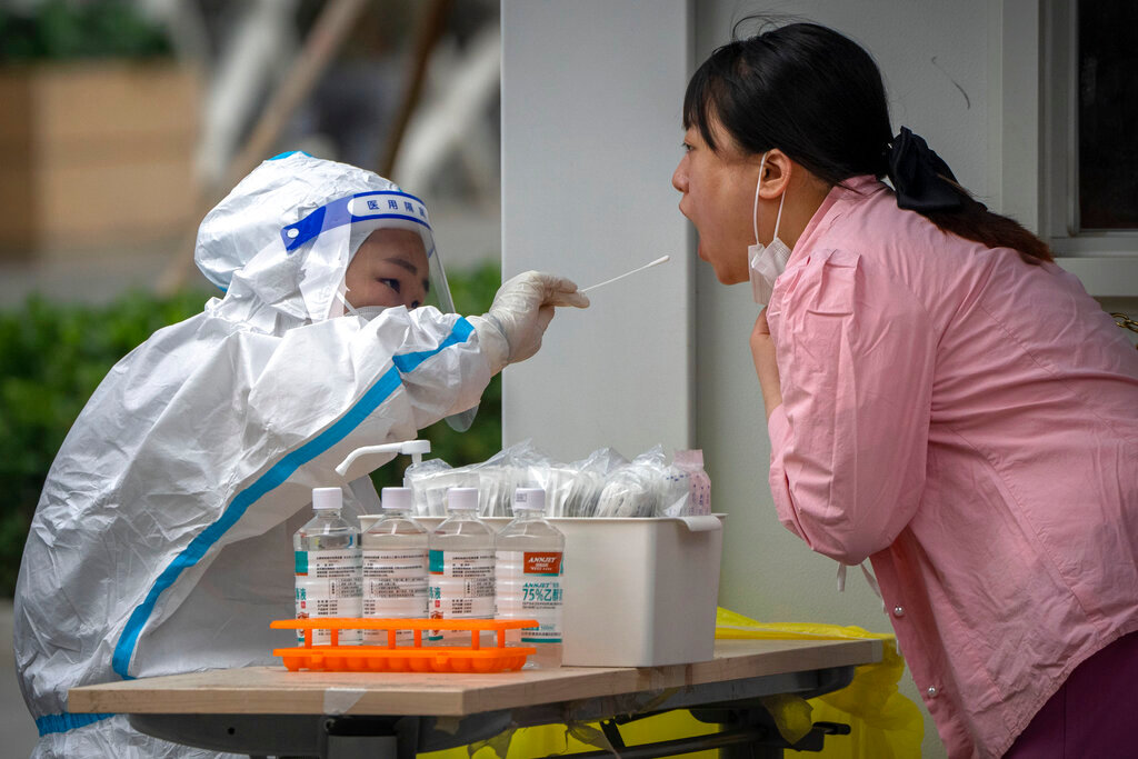 A worker wearing a protective suit swabs a woman's throat for a COVID-19 test at a coronavirus testing site in Beijing, Thursday, June 9, 2022. (AP Photo/Mark Schiefelbein)