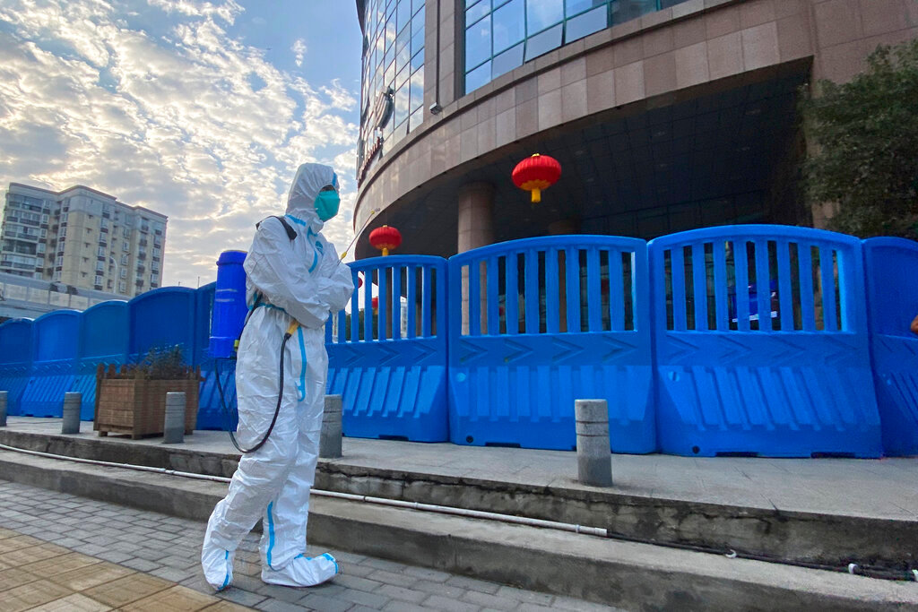 A worker in protective overalls and carrying disinfecting equipment walks outside the Wuhan Central Hospital, China on Feb. 6, 2021. (AP Photo/Ng Han Guan, File)