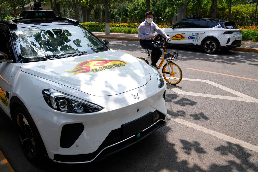 A man cycles past self-driving taxis developed by tech giant Baidu Inc. on June 14, 2022, in Beijing. (AP Photo/Ng Han Guan)