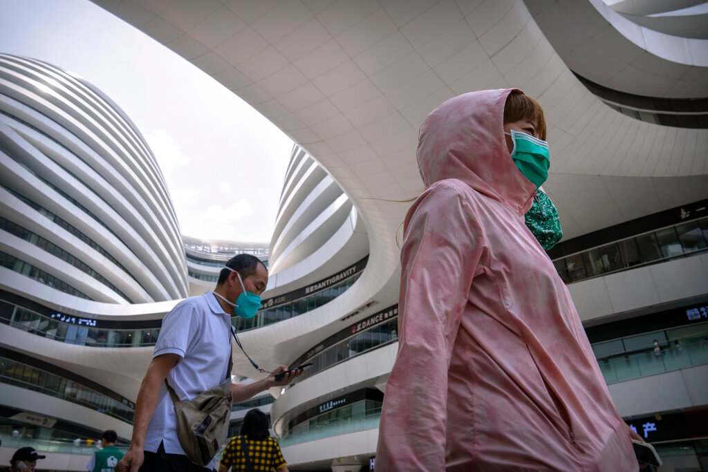 People wearing face masks walk through a shopping and office complex in Beijing, Thursday, June 30, 2022. (AP Photo/Mark Schiefelbein)