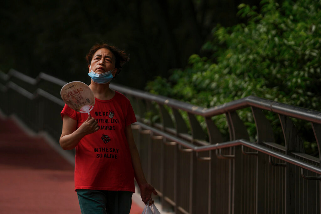 A woman fans herself as she walks on a pedestrian bridge in Beijing, Tuesday, July 5, 2022. (AP Photo/Andy Wong)