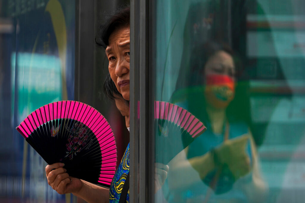 A woman fans herself at a bus stand as she waits in Beijing, Tuesday, July 5, 2022. (AP Photo/Andy Wong)