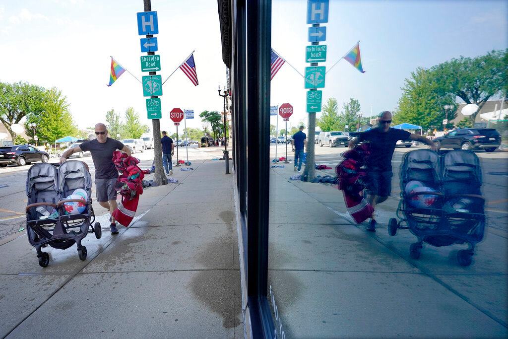 Highland Park, Ill., resident Murry Rosenbush is reflected in a store window as he removes items left behind by attendees to the town's Fourth of July parade Tuesday, July 5, 2022. (AP Photo/Charles Rex Arbogast)