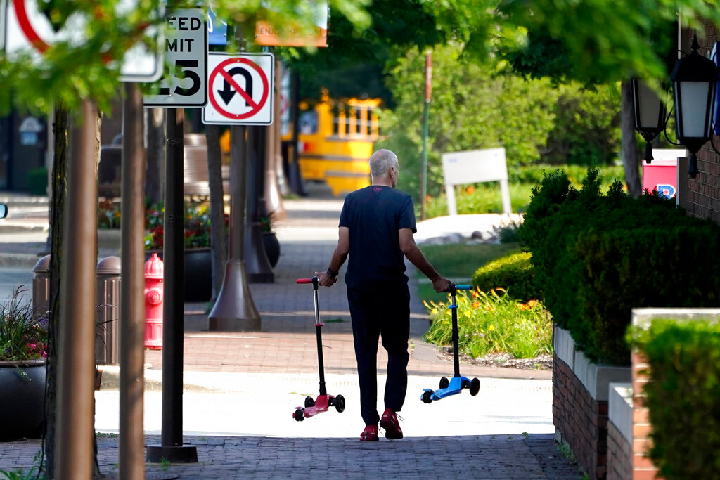 A man removes two children's scooters one day after a mass shooting in downtown Highland Park, Ill., Tuesday, July 5, 2022. (AP Photo/Charles Rex Arbogast)