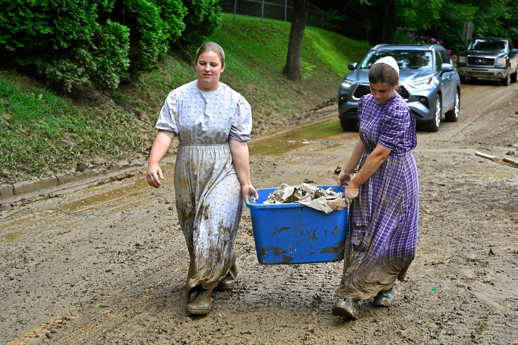 Volunteers from the local mennonite community carry tubfulls of debris from flood soaked houses for disposal at Ogden Hollar in Hindman, Ky., Saturday, July 30, 2022. (AP Photo/Timothy D. Easley)