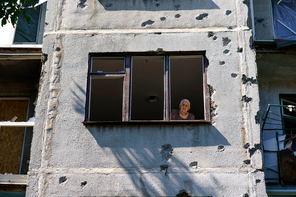 An elderly woman looks out of her apartment window in a building damaged in a May rocket attack in Sloviansk, Donetsk region, eastern Ukraine, Saturday, Aug. 6, 2022. (AP Photo/David Goldman)