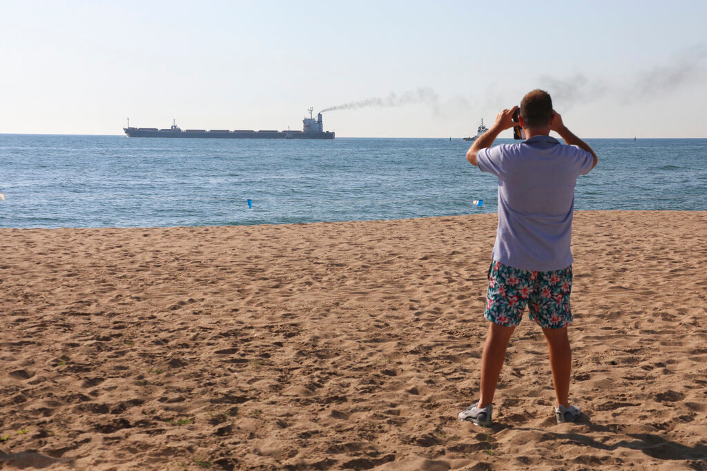 A man takes a picture as the Glory bulk carrier makes its way from the port in Odesa, Ukraine, Sunday, Aug. 7, 2022. According to Ukraine's Ministry of Infrastructure, the ship is carrying 66,000 tons of Ukrainian corn. (AP Photo/Nina Lyashonok)