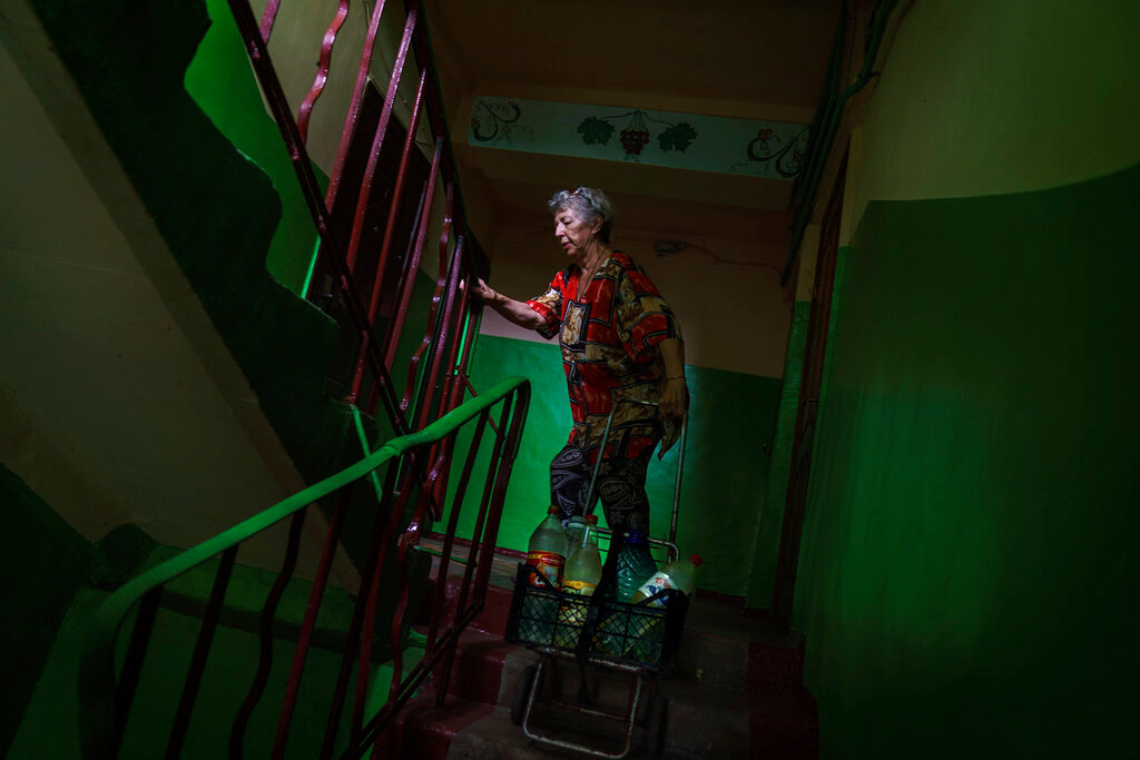 Lyubov Mahlii, 76, pulls a crate of water bottles up the stairs to her fifth-floor apartment after filling them up at a nearby park in Sloviansk, Donetsk region, eastern Ukraine, Saturday, Aug. 6, 2022. (AP Photo/David Goldman)