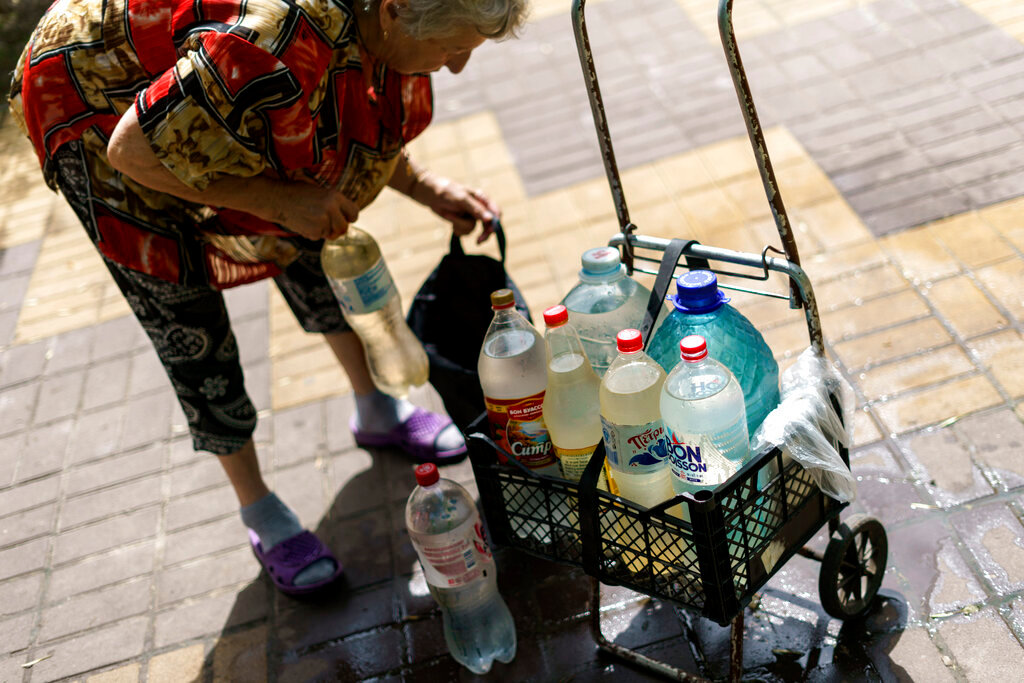 Lyubov Mahlii, 76, packs a crate with water bottles she filled up at a public tank to take back to her apartment in Sloviansk, Donetsk region, eastern Ukraine, Saturday, Aug. 6, 2022. (AP Photo/David Goldman)