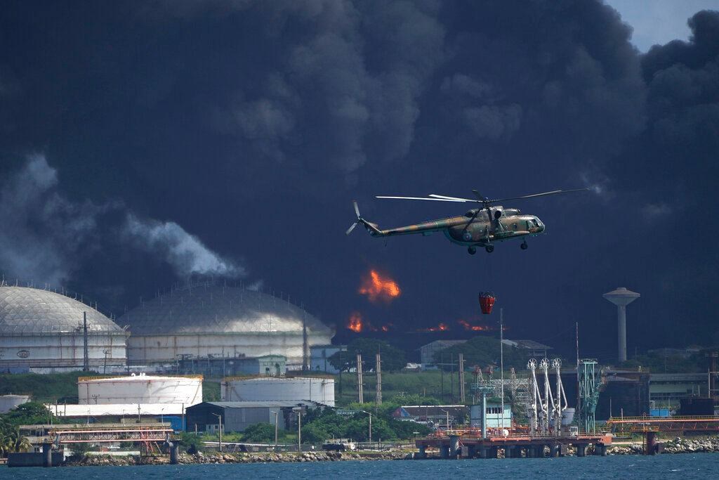 A helicopter carrying water flies over the Matanzas Supertanker Base, as firefighters try to quell the blaze which began during a thunderstorm the night before, in Matazanas, Cuba, Saturday, Aug. 6, 2022. (AP Photo/Ramon Espinosa)