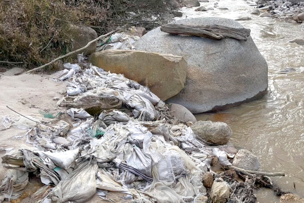 A creek in Myanmar's Kachin State is lined with trash, pipes and other construction materials from a former rare earth mining site. Local villagers have said water from the creek is no longer usable for drinking or growing crops and that their skin itches after being exposed to the water near rare earth mining sites. (Global Witness via AP)