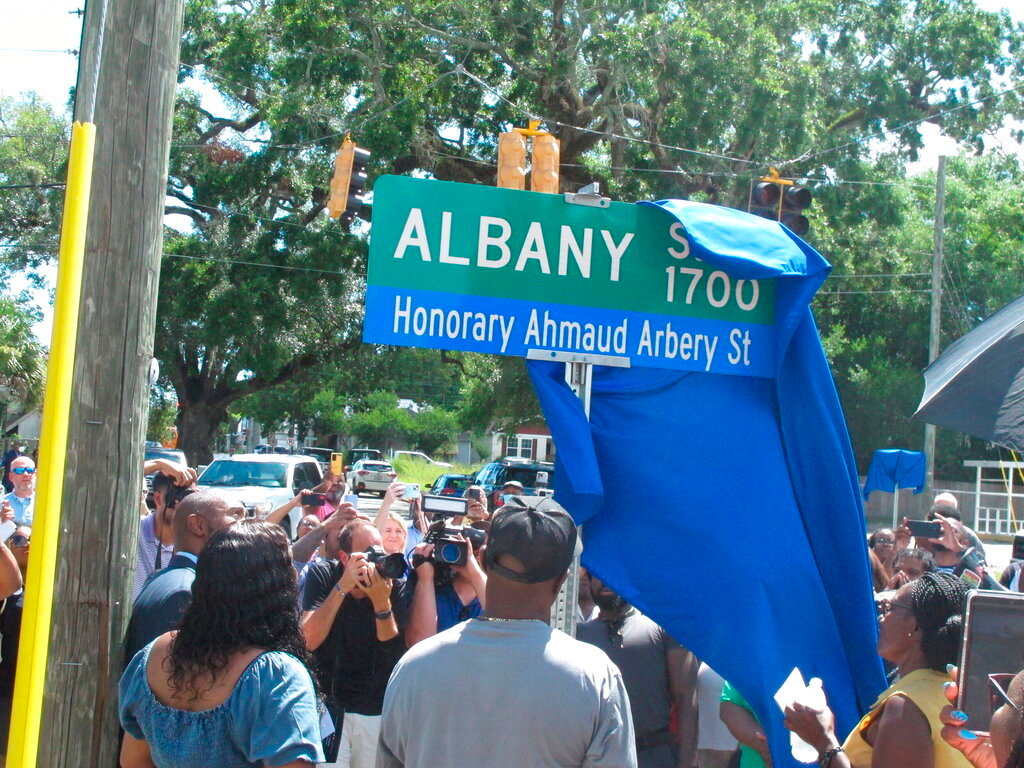 A blue covering is pulled aside to unveil a new street sign designating Albany St. as Honorary Ahmaud Arbery St. in Brunswick, Georgia, on Tuesday, Aug. 9, 2022. (AP Photo/Russ Bynum)