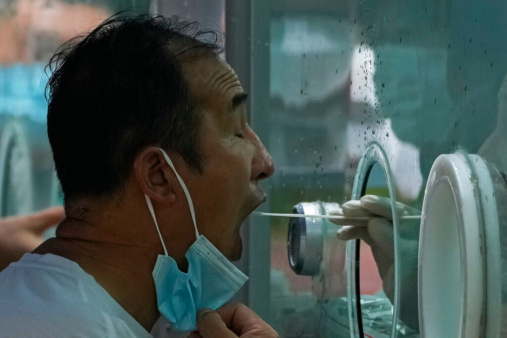 A man pulls his mask to get his routine COVID-19 throat swab at a coronavirus testing site in Beijing, Tuesday, Aug. 9, 2022. (AP Photo/Andy Wong)