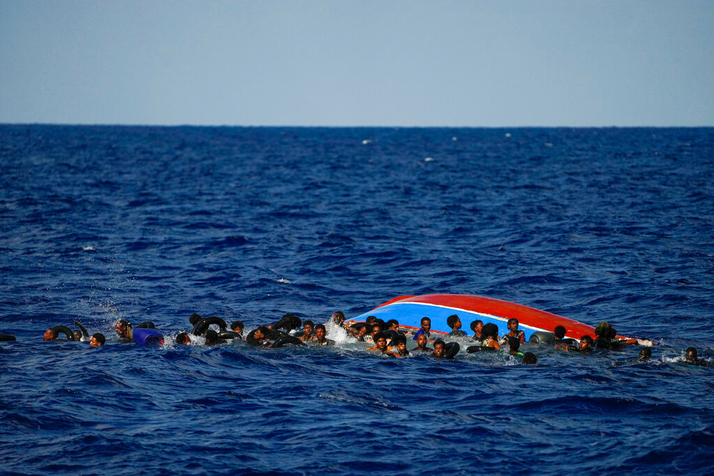 Migrants swim next to their overturned wooden boat during a rescue operation by Spanish group Open Arms south of Lampedusa island in the Mediterranean sea Thursday, Aug. 11, 2022. (AP Photo/Francisco Seco)