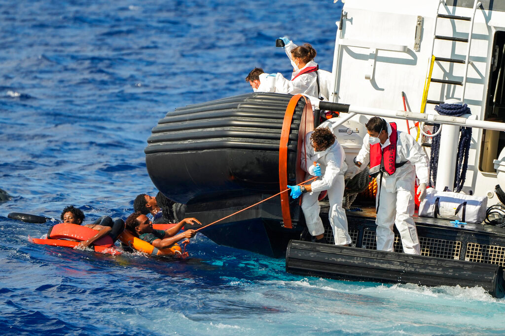 Italian coast guard members help migrants after their wooden boat overturned during a rescue operation south of Lampedusa island in the Mediterranean sea Thursday, Aug. 11, 2022. (AP Photo/Francisco Seco)
