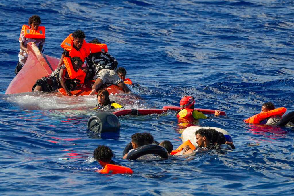 Lifeguards with Spanish group Open Arms help migrants after their wooden boat overturned during a rescue operation south of Lampedusa island in the Mediterranean sea Thursday, Aug. 11, 2022. (AP Photo/Francisco Seco)