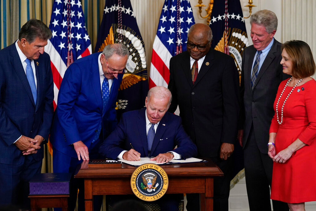 President Joe Biden signs the Democrats' landmark climate change and health care bill in the State Dining Room of the White House in Washington, Tuesday, Aug. 16, 2022, as from left, Sen. Joe Manchin, D-W.Va., Senate Majority Leader Chuck Schumer of N.Y., House Majority Whip Rep. James Clyburn, D-S.C., Rep. Frank Pallone, D-N.J., and Rep. Kathy Castor, D-Fla., watch. (AP Photo/Susan Walsh)