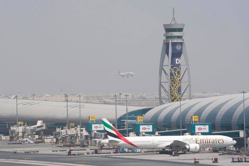 An Emirates Boeing 777 sits at the gate at Dubai International Airport as another prepares to land on the runway in Dubai, United Arab Emirates, Wednesday, Aug. 17, 2022. (AP Photo/Jon Gambrell)
