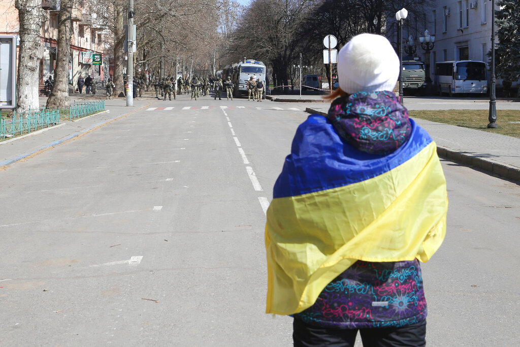 A woman covered by Ukrainian flag stands in front of Russian troops in a street during a rally against Russian occupation in Kherson, Ukraine, March 19, 2022.  (AP Photo/File)