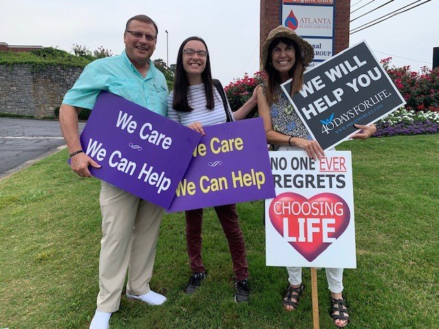 Mike Griffin, Rachel Guy and Suzanne Guy, from left, hold signs in front of an abortion clinic in July 2021.