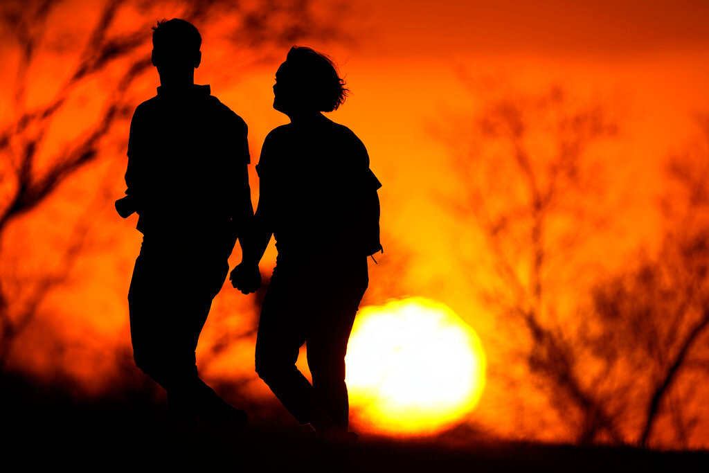 A couple walks through a park at sunset in Kansas City, Mo. (AP Photo/Charlie Riedel, File)