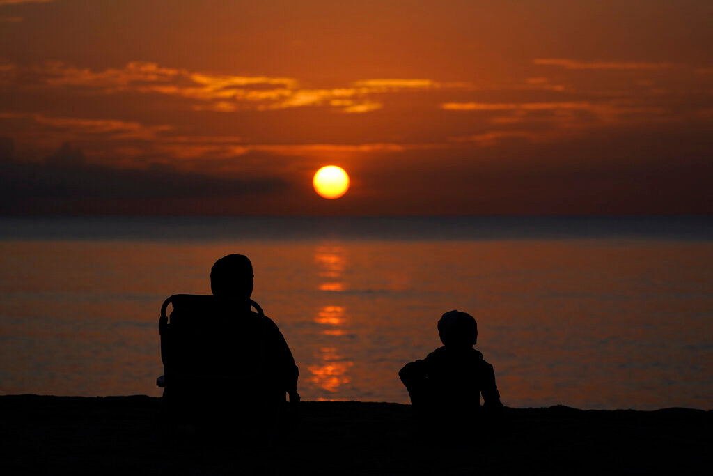 A pair of beachgoers watch the sun rise over the Atlantic Ocean, June 10, 2022, in Surfside, Fla. (AP Photo/Wilfredo Lee, File)