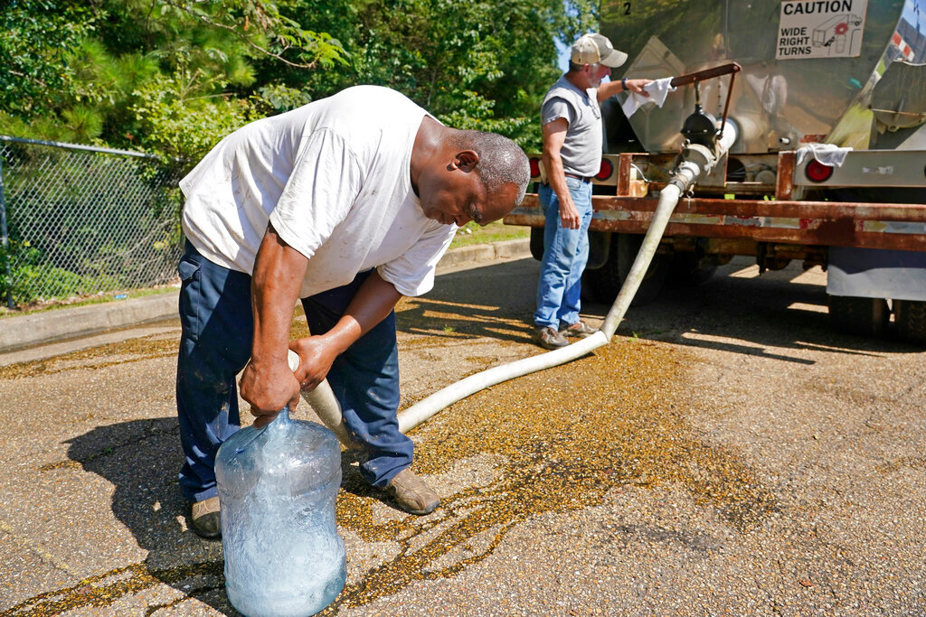 Ty Carter, right, and Benjamin Williams, with Garrett Enterprises, fill up a five-gallon jug for an area resident from a water tanker at Forest Hill High School in Jackson, Miss., Wednesday, Aug. 31, 2022. (AP Photo/Rogelio V. Solis)