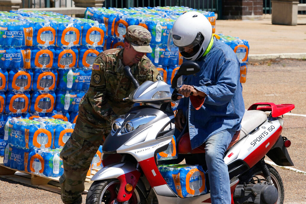 A member of the Mississippi National Guard places a case of water on the scooter of Jackson resident Keith Angeleti near downtown Jackson, Miss., Thursday, Sept. 1, 2022. (AP Photo/Steve Helber)