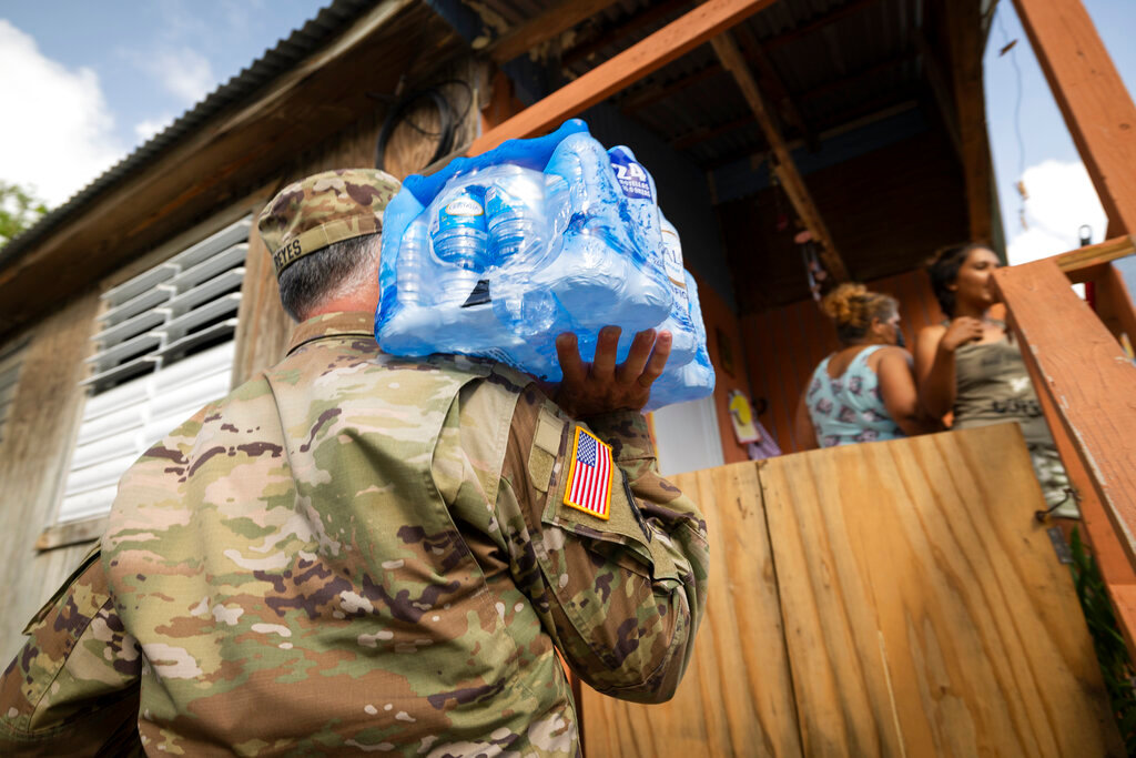 A National Guardsman delivers water to the residents of Punta Diamante in Ponce, Puerto Rico, Wednesday, Sept. 21, 2022. (AP Photo/Alejandro Granadillo)