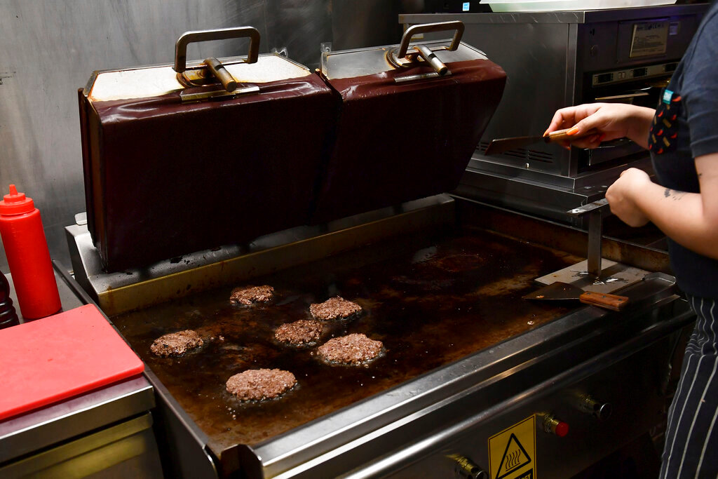 A worker cooks burgers at Zing Burger store in Budapest, Hungary, Monday, Sept. 12, 2022. Richard Kovacs, a business development manager for the Hungarian burger chain, said some of the chain's 15 stores have seen a 750% increase in electricity bills since the beginning of the year. (AP Photo/Anna Szilagyi)