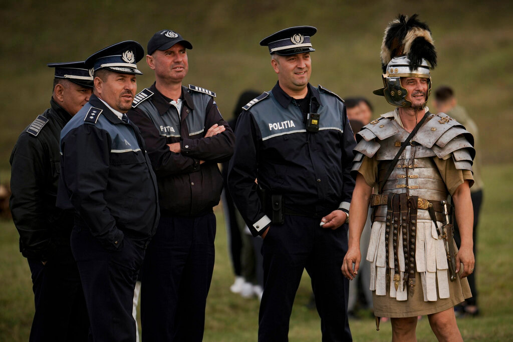 Police officers watch reenactments of Roman Empire era gladiator fights standing next to a participant dressed as a Roman soldier in the village of Resca, Romania, Saturday, Sept. 3, 2022. (AP Photo/Vadim Ghirda)