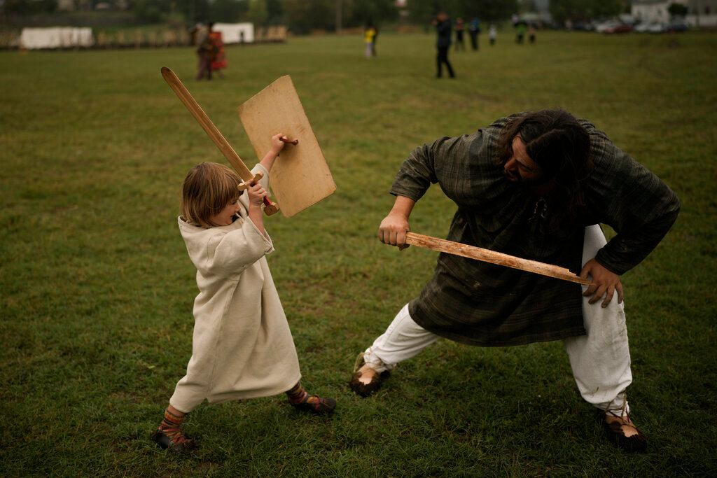 A man and child, participants in the Romula Fest historic reenactment event fight with wooden swords in the village of Resca, Romania, Saturday, Sept. 3, 2022. (AP Photo/Andreea Alexandru)