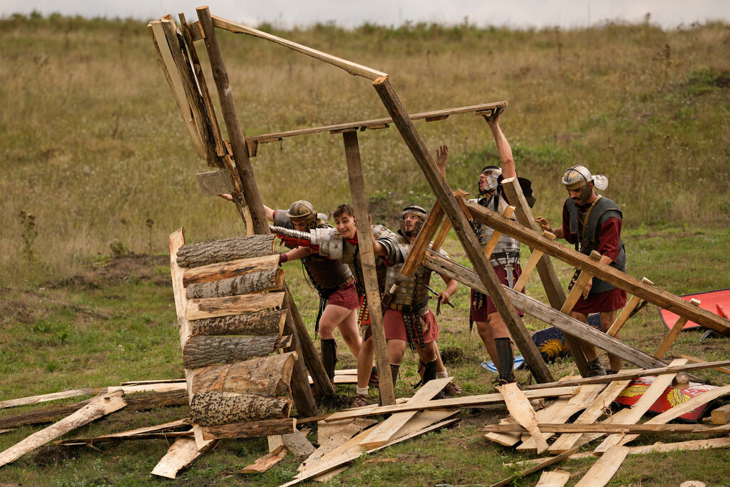 Men wearing Roman soldiers' outfits destroy a wooden structure during the Romula Fest historic reenactment event in the village of Resca, Romania, Sunday, Sept. 4, 2022. (AP Photo/Andreea Alexandru)