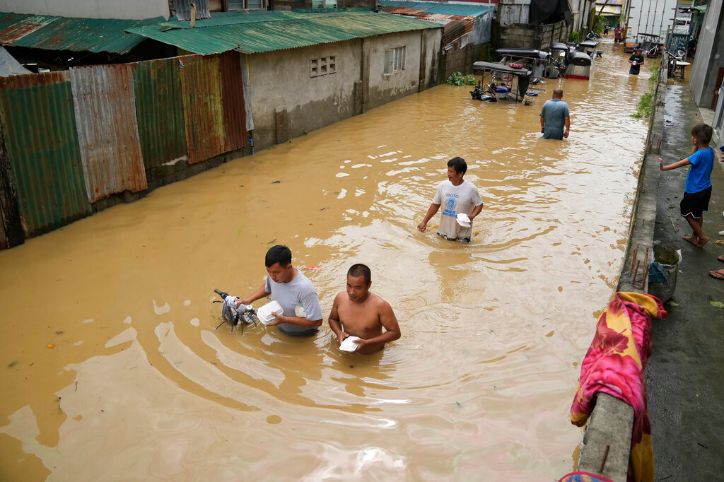 Residents carrying food packs wade along a flooded street from Typhoon Noru in San Miguel, Bulacan province, Philippines, Monday, Sept. 26, 2022. (AP Photo/Aaron Favila)