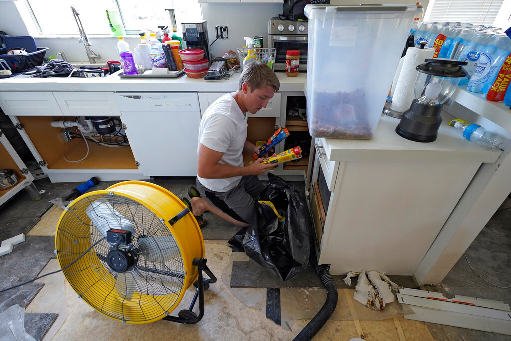Jordan Cromer cleans water-logged items at his home, Tuesday, Oct. 4, 2022, in North Port, Fla. (AP Photo/Chris O'Meara)