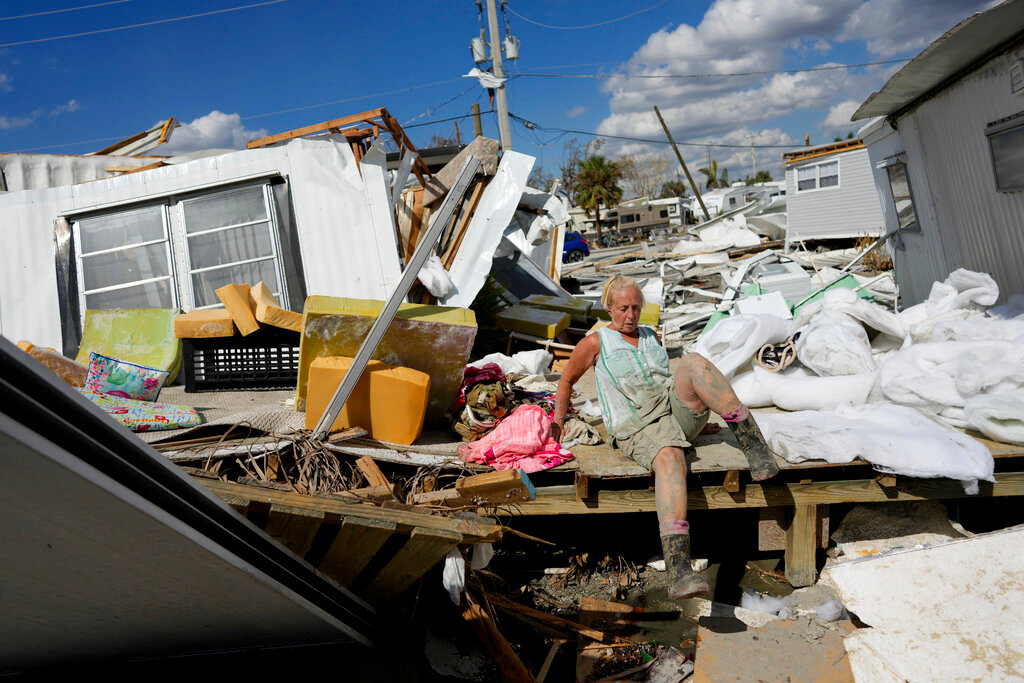 Kathy Hickey, 70, carefully climbs across a ruined trailer as she picks her way through debris to where she and her husband Bruce had a winter home, a trailer originally purchased by Kathy's mother in 1979, on San Carlos Island in Fort Myers Beach, Fla., Wednesday, Oct. 5, 2022, one week after the passage of Hurricane Ian. (AP Photo/Rebecca Blackwell)