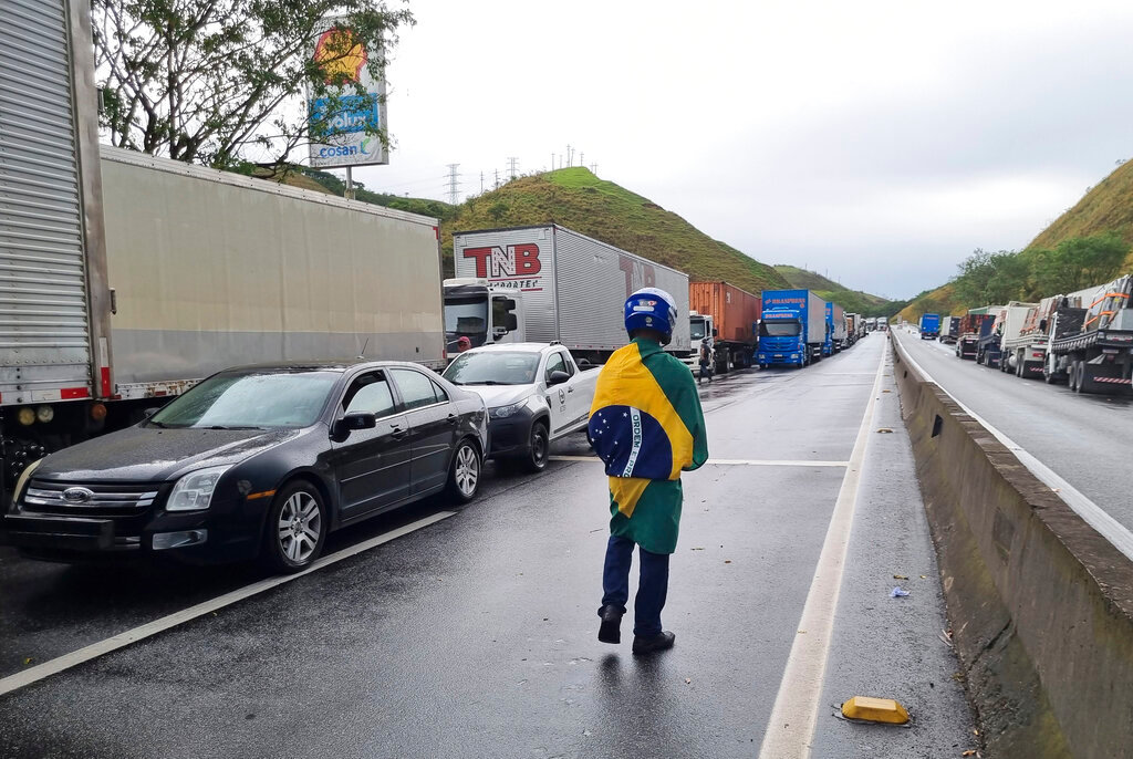A truck driver wearing a Brazilian flag walks past cargo trucks standing idle on the Rio de Janeiro-Sao Paulo highway, parked to protest the previous day's election defeat of President Jair Bolsonaro, in Barra Mansa, Rio de Janeiro state, Brazil, Monday, Oct. 31, 2022. (AP Photo/Rodrigues Da Silva)