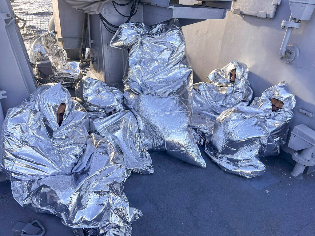 Some of the nine men who survived a shipwreck and were found on an uninhabited islet are covered with thermal blankets as they sit aboard a Greek Coast guard vessel, in the Aegean Sea, Greece, on Tuesday, Nov. 1, 2022. (Greek Coast Guard via AP)