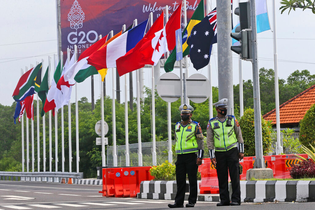 Police officers stand guard as flags of G20 countries wave on a road leading to the venue of the G20 Summit in Nusa Dua, Bali, Indonesia on Saturday, Nov. 12, 2022. A showdown between Presidents Joe Biden and Vladimir Putin isn't happening, but the fallout from Russia's invasion of Ukraine and growing tensions between China and the West will be at the forefront when leaders of the world's biggest economies gather in tropical Bali this week.(AP Photo/Firdia Lisnawati)