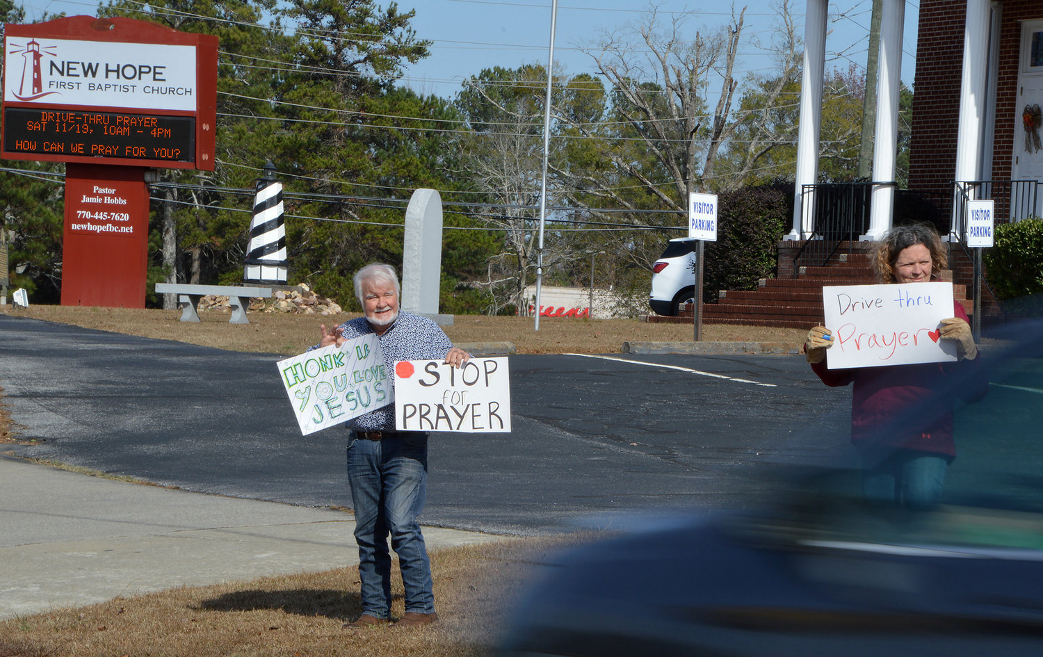 Bill Lloyd waves to a honking motorist while holding signs encouraging people to pull into New Hope First Baptist Church for drive-thru prayer on Saturday, Nov. 19, 2022, in Dallas, Ga. Lloyd's wife Debbie is at right. (Index/Henry Durand)