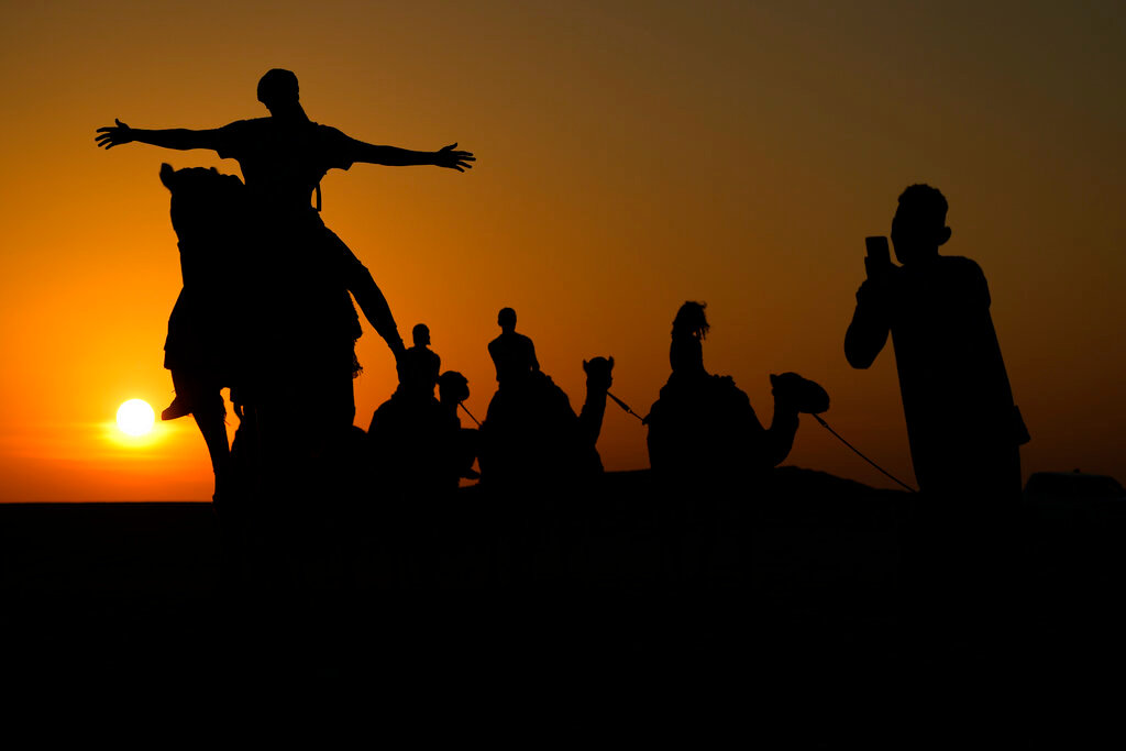 A man has his photo taken atop a camel in Mesaieed, Qatar, Nov. 26, 2022. (AP Photo/Ashley Landis)