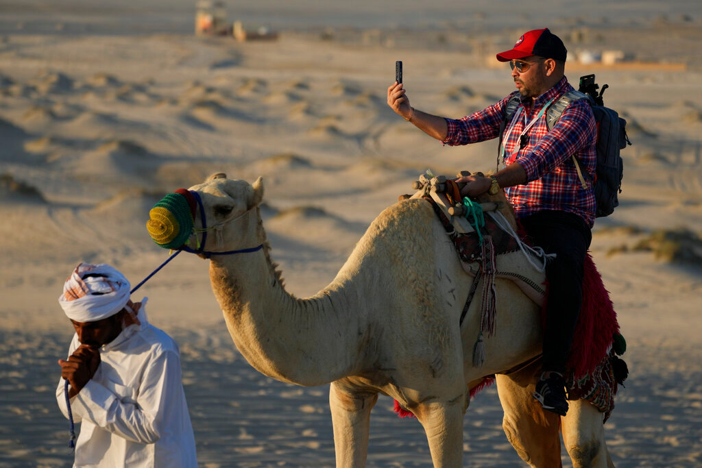 A man takes a selfie while riding camels in Mesaieed, Qatar, Nov. 26, 2022. (AP Photo/Ashley Landis)