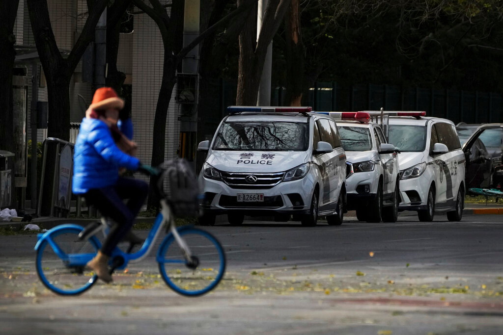 A woman rides past police vehicles parked along a road near the site of last weekend's protest in Beijing, Tuesday, Nov. 29, 2022. (AP Photo/Andy Wong)