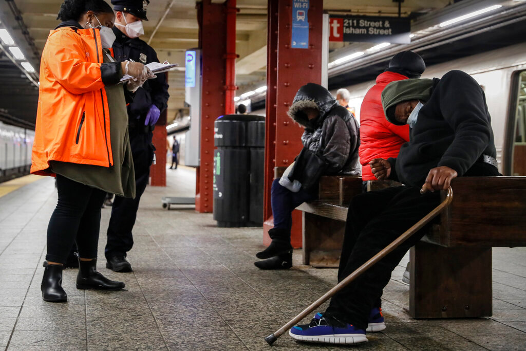 A homeless outreach worker and a New York police officer assist passengers found sleeping on subway cars at the 207th Street A-train station, April 30, 2020, in the Manhattan borough of New York. (AP Photo/John Minchillo, File)