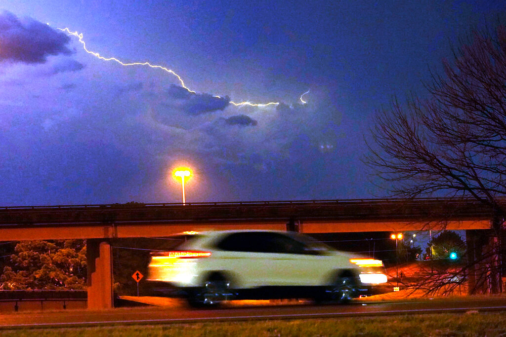 A vehicle races along a Jackson, Miss., street as lightning streaks across the sky, Tuesday evening, Nov. 29, 2022. (AP Photo/Rogelio V. Solis)