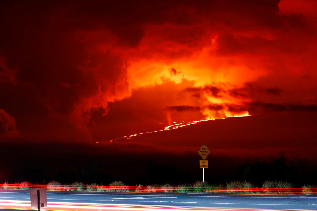 Cars drive down Saddle Road as Mauna Loa erupts in the distance, Monday, Nov. 28, 2022, near Hilo, Hawaii. (AP Photo/Marco Garcia)