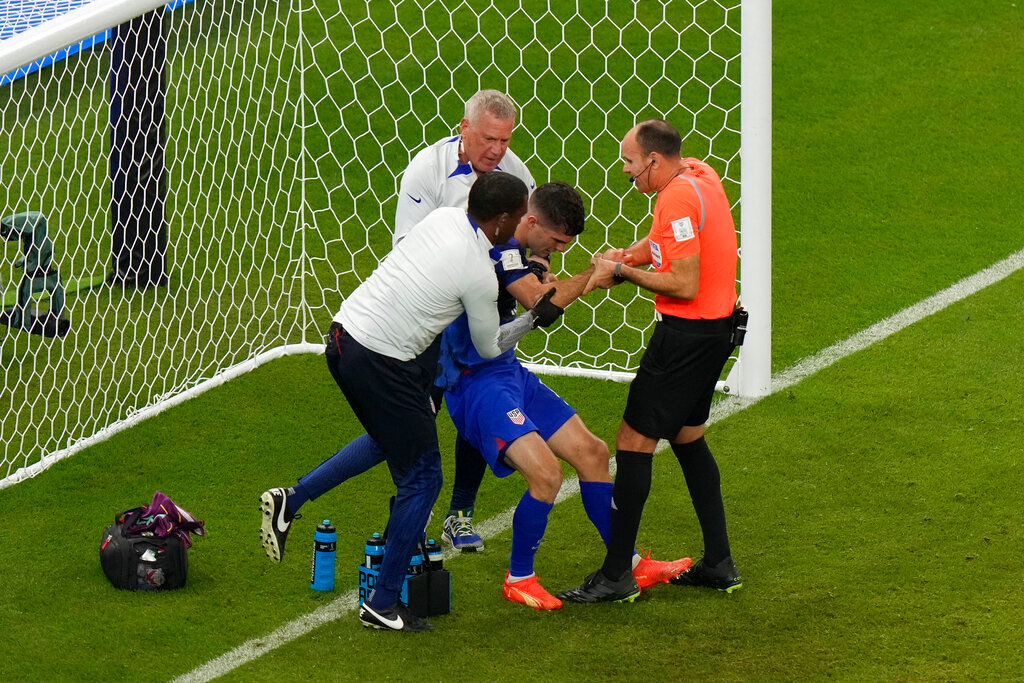 Christian Pulisic of the United States is helped by referee Antonio Mateu, of Spain, and team doctors after he scoring his side's opening goal during a World Cup group B soccer match against Iran in Doha, Qatar, Tuesday, Nov. 29, 2022. (AP Photo/Luca Bruno)