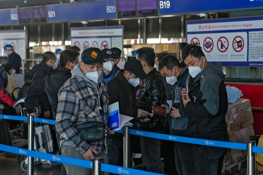 Masked travelers check their passports as they line up at the international flight check-in counter at the Beijing Capital International Airport in Beijing, Thursday, Dec. 29, 2022. (AP Photo/Andy Wong)