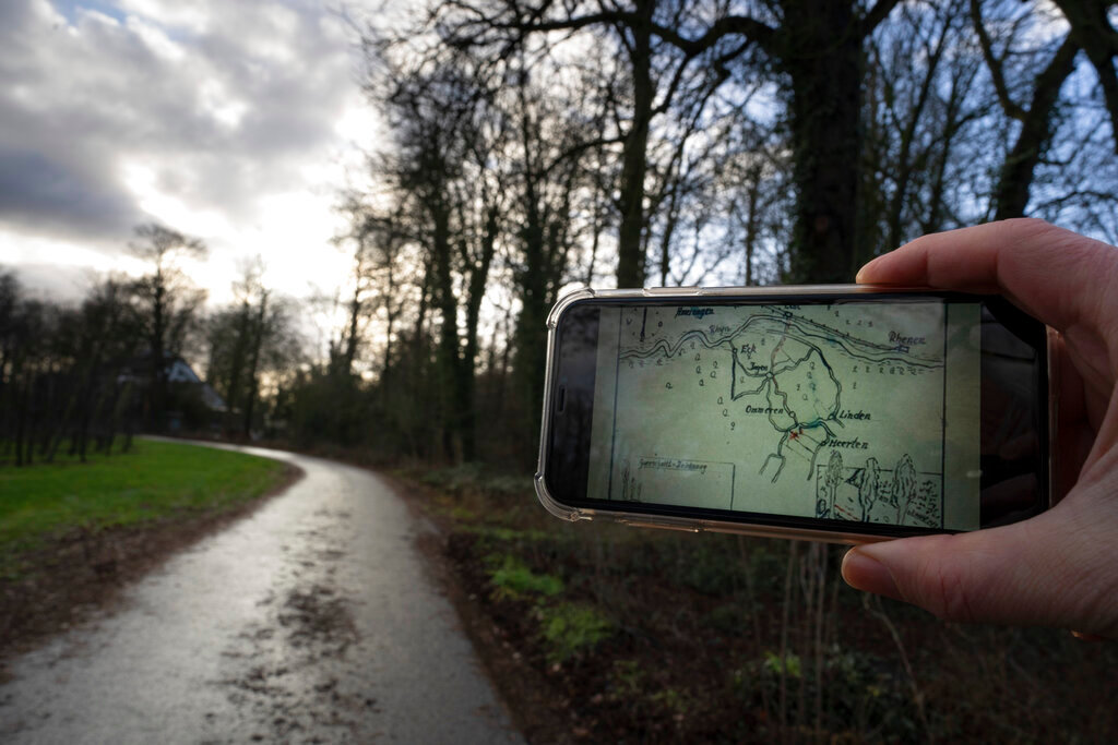 A cameraman holds a mobile phone showing a map of the buried Nazi loot on the location of the former dirt road in Ommeren, near Arnhem, Netherlands, Thursday, Jan. 19, 2023. (AP Photo/Peter Dejong)
